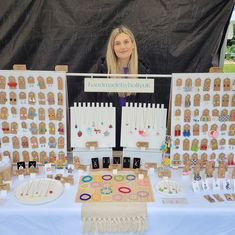 a woman standing in front of a table with lots of earrings on it and an assortment of necklaces