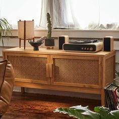 an old radio sits on top of a wooden cabinet in front of a window with potted plants