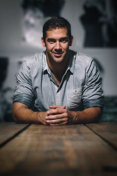 a man sitting at a wooden table with his hands folded in front of the camera