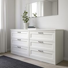 a white dresser with two drawers and a plant in the corner on top of it