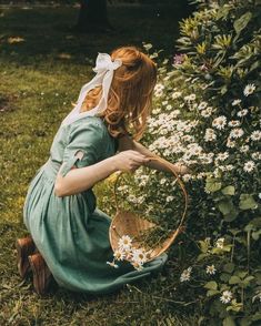 a woman kneeling down in the grass with a basket on her lap and daisies around her