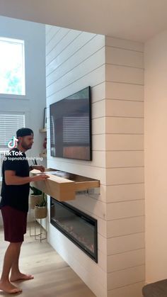 a man standing in front of a flat screen tv next to a wall mounted fireplace