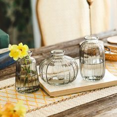 three glass vases sitting on top of a wooden table next to a yellow flower