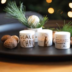 three white candles sitting on top of a wooden table next to nuts and pine cones