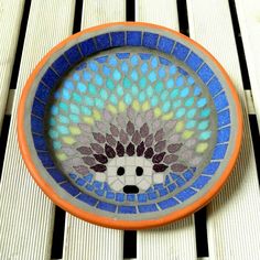 an orange and blue bowl with a mosaic design on the front is sitting on a wooden table