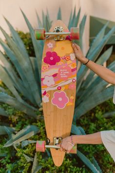 a woman holding up a skateboard in front of some bushes and plants with her hand on the board