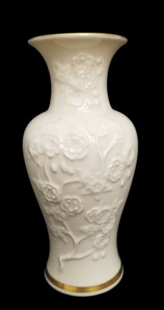 a white vase with gold trimmings on the bottom is shown in front of a black background