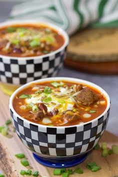 two bowls of chili soup with meat and cheese on the top, sitting on a cutting board