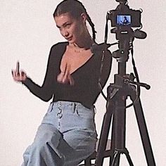 a woman standing in front of a tripod with her hand up to the camera