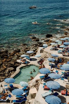 people are lounging on the beach with blue umbrellas and sunbathers in the water