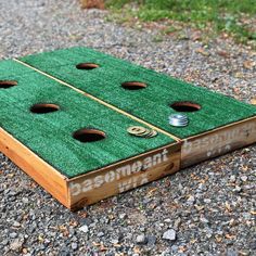 a wooden board game set up on gravel with coins in the hole and words underneath it