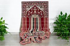 a red rug with an intricate design on the floor next to potted plants and greenery