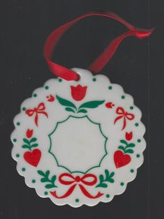 a christmas ornament hanging from a red ribbon on a black surface with white and green designs