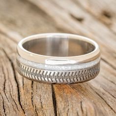 a wedding band with a baseball pattern on it sitting on a piece of drift wood