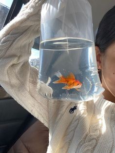 a woman holding up a fish bowl with goldfish in it and wearing a sweater