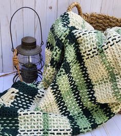 a green and white crocheted blanket sitting on top of a wooden floor next to a lantern