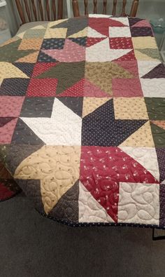 a table with a quilt on it and some chairs in front of the table top