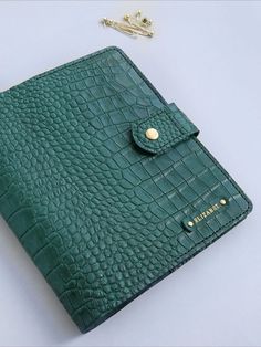 a green alligator skin wallet with a chain attached to the front and side, sitting on a white surface