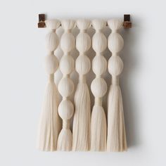 a wall hanging made out of wooden beads and tassels on a white wall