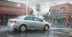 a silver car driving down a street next to tall buildings and palm trees in the rain