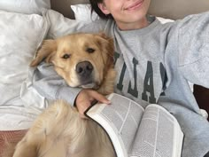 a woman is laying in bed with her dog and reading a book while wearing a sweatshirt