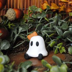 a small white ghost sitting on top of a wooden table next to leaves and pumpkins