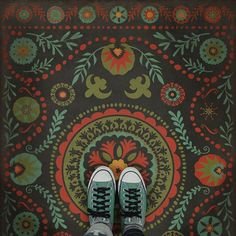 a person standing in front of a colorful rug with shoes on the floor and their feet propped up