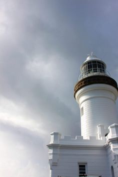 a large white lighthouse with a clock on it's side under a cloudy sky