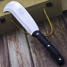 a large knife sitting on top of a wooden table next to a box and rope