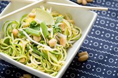 a white bowl filled with noodles and vegetables on top of a blue table cloth next to chopsticks