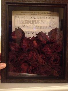 someone is holding up a frame with sheet music and dried roses in it as if they were playing the piano