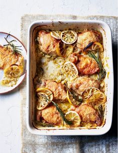 a casserole dish with chicken, lemons and rosemary garnishes