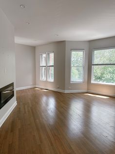 an empty living room with hard wood flooring and two windows in the back wall