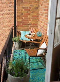 a balcony with chairs, table and potted plants on the outside patio area in front of brick building