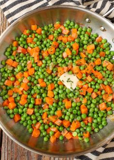 peas, carrots and butter in a pan on top of a striped towel next to a wooden table