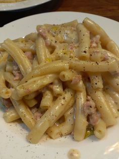 a white plate topped with pasta covered in meat and sauces on top of a wooden table