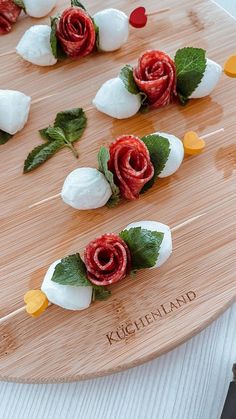 there are marshmallows and roses on the wooden platter with green leaves