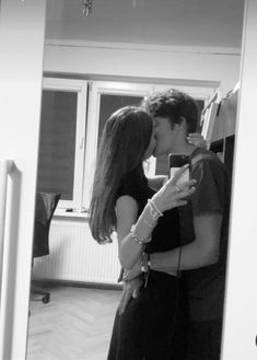 a man and woman kissing in front of a mirror while holding a cell phone to their ear