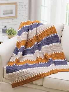 a crocheted blanket sitting on top of a white couch next to a window