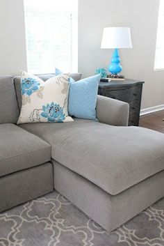 a living room with a gray sectional couch and blue pillows on the back of it