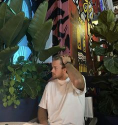 a man sitting in front of a potted plant with his hand on his head