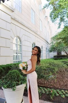 a woman standing in front of a white building holding a bouquet of flowers and smiling