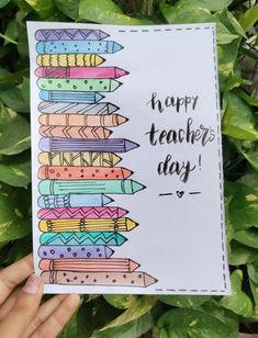 a hand holding up a card that says happy teacher's day with colorful crayons