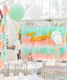 an indoor party with balloons and streamers on the wall, table cloths and chairs