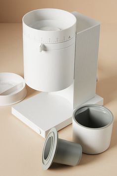 an assortment of white objects are arranged on a beige surface, including a coffee maker and two mugs