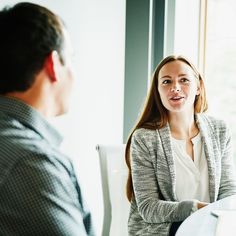 a woman sitting at a table talking to a man who is wearing a blazer