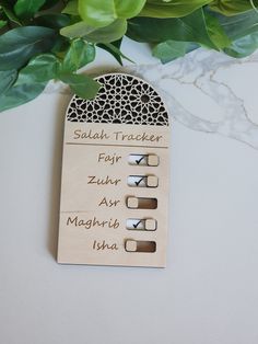 a wooden name tag with arabic writing on it next to some green plants and leaves