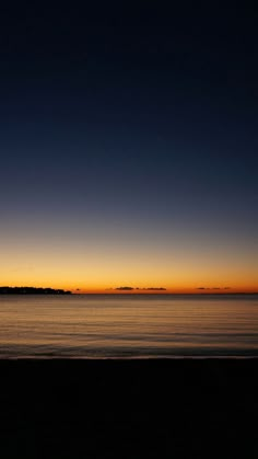 the sun is setting over the ocean and there are two people walking on the beach