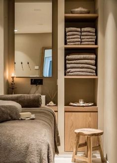 a bed sitting next to a wooden shelf filled with towels