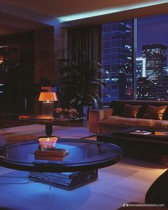 a living room filled with furniture and tall buildings in the background at night, lit up by blue lights